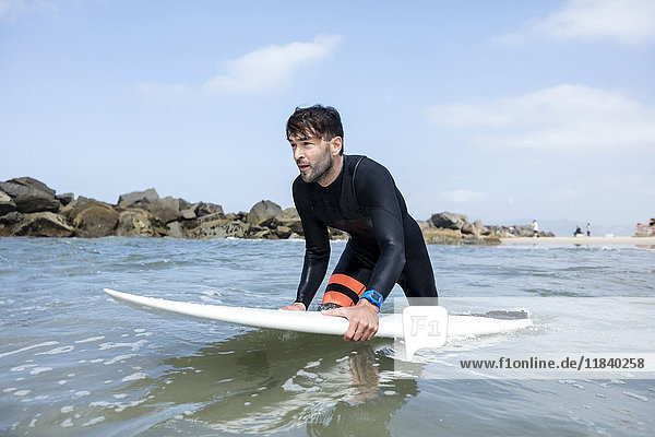 Kaukasischer Mann watet im Meer und hält ein Surfbrett