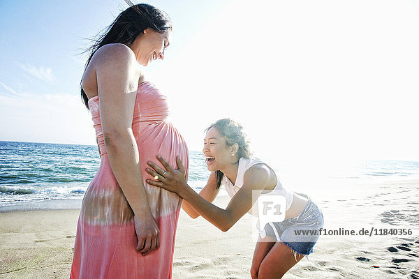 Woman holding belly of expectant mother at beach