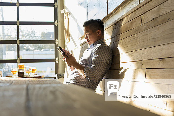 Asiatischer Mann  der in einer Brauereikneipe eine SMS auf seinem Handy schreibt