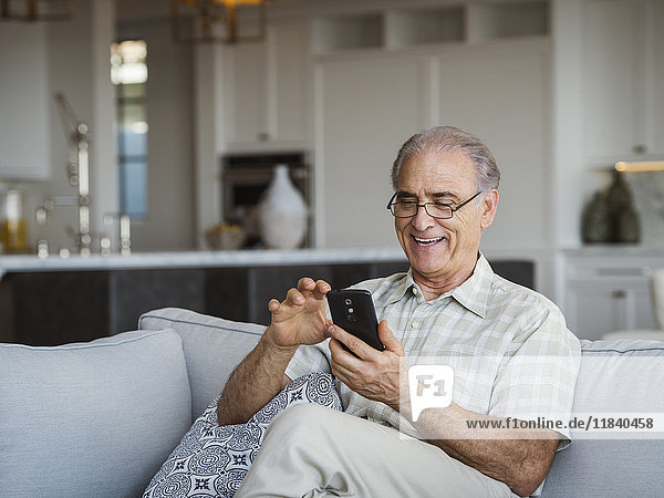 Caucasian man sitting on sofa texting on cell phone
