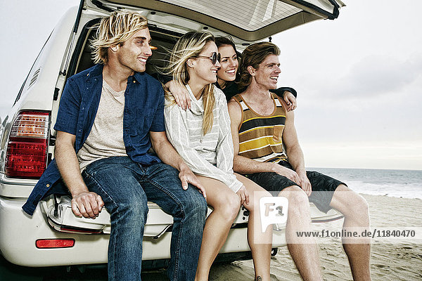 Caucasian friends sitting in car hatch at beach
