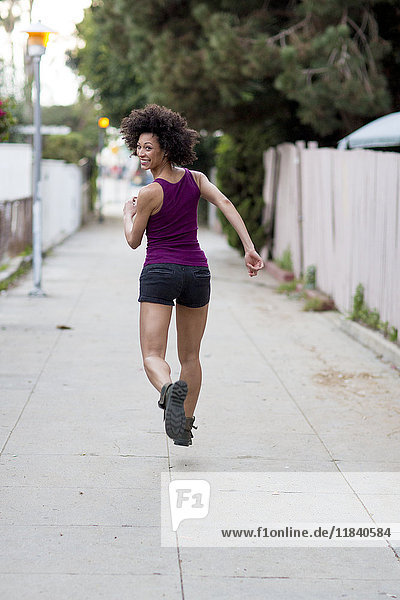 Smiling Mixed Race woman running on sidewalk