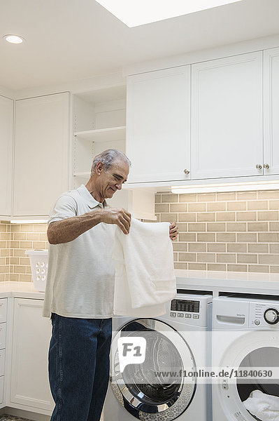 Kaukasischer Mann faltet Handtuch in moderner Waschküche