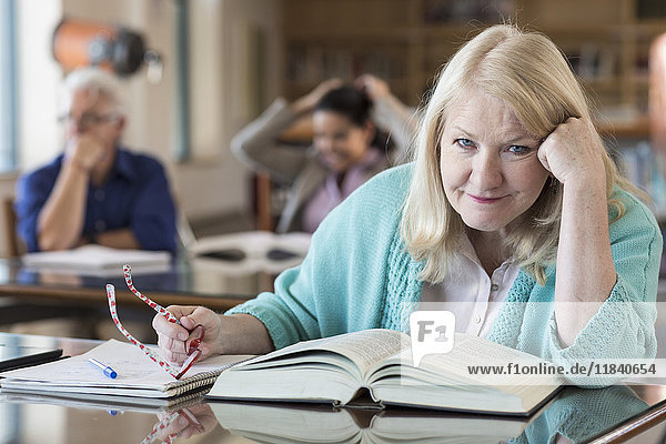 Verwirrte ältere Frau  die in einer Bibliothek ein Buch liest