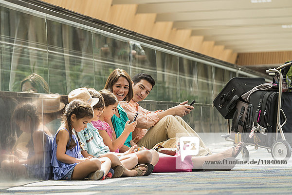Familie wartet auf dem Boden des Flughafens und benutzt Handys