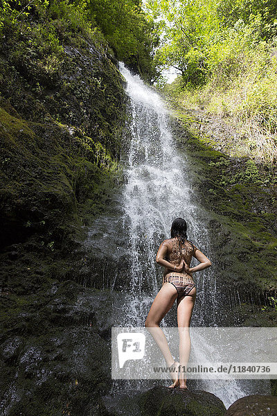 Kaukasische Frau steht auf einem Felsen in der Nähe eines Wasserfalls und macht Yoga