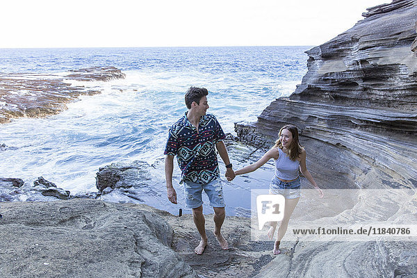 Lächelndes Paar  das am Strand auf Felsformationen spazieren geht