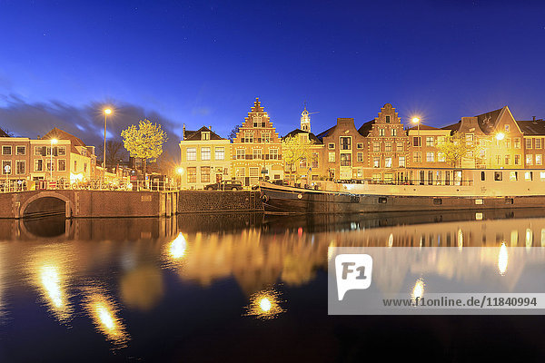Dusk lights on typical houses and bridge reflected in a canal of the River Spaarne  Haarlem  North Holland  The Netherlands  Europe