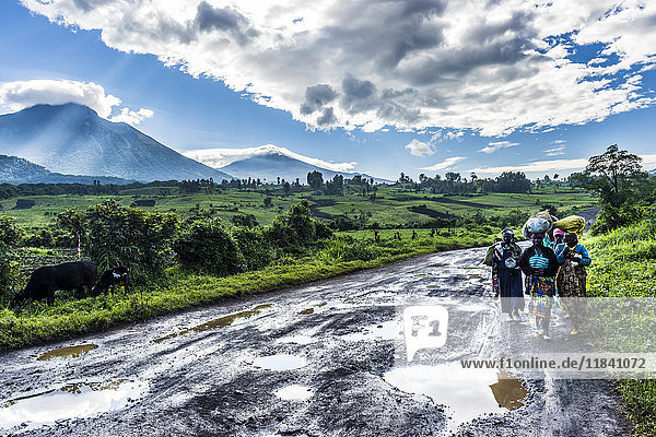 Local women carrying goods on their heads with the volcanic mountain chain of the Virunga National Park behind  after rain  Democratic Republic of the Congo  Africa