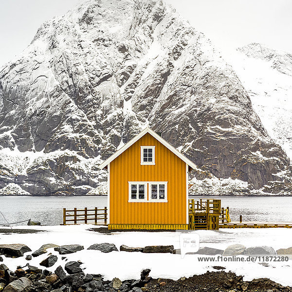 Ein leuchtend gelbes Gebäude am Wasser mit einem schneebedeckten Berg im Hintergrund; Nordland,  Norwegen'.