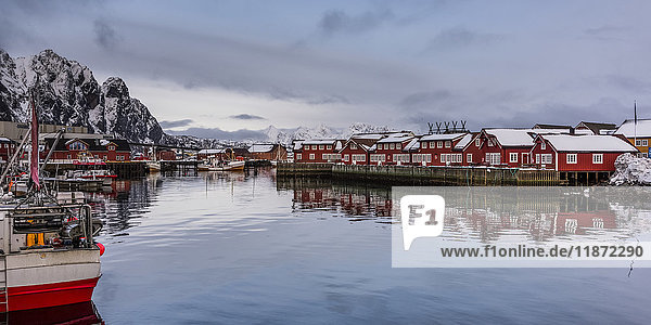 Rote Gebäude säumen die Wasserkante und spiegeln sich im ruhigen Wasser mit Booten  die entlang der Uferlinie vertäut sind; Svolvar  Lofoten  Nordland  Norwegen'.