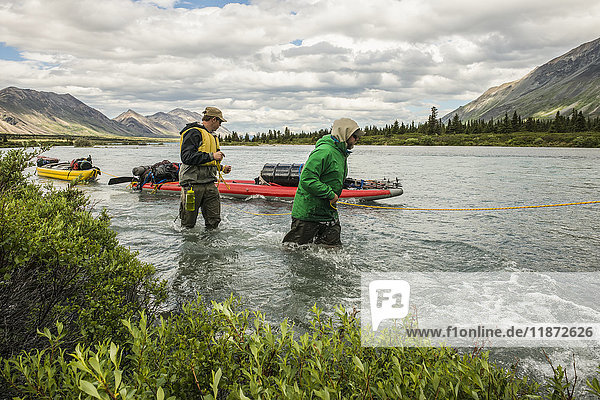 A pair of backcountry travelers line kayaks up a stream in the Twin Lakes area of Lake Clark National Park & Preserve  Southcentral Alaska  USA