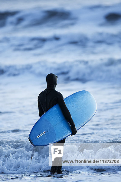 Surfer  der mit seinem Brett am Rande des Wassers steht  Homer Spit  Kachemak Bay  Kenai Peninsula  Southcentral Alaska  USA