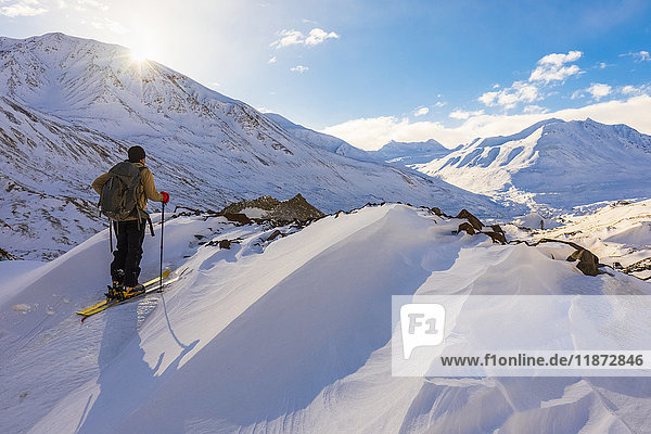 'A backcountry skier looks over the Black Rapids Glacier valley from a high point on the terminal moraine in winter; Alaska  United States of America'