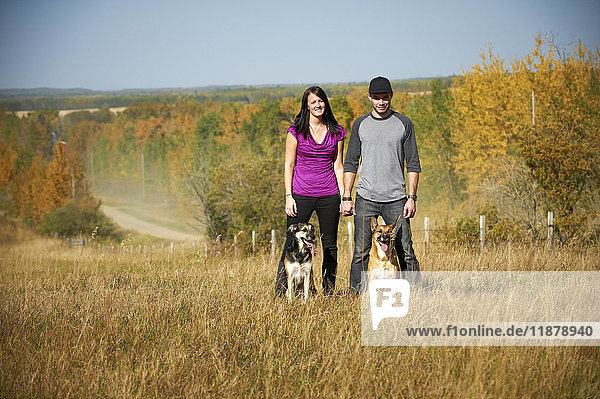 'Portrait of a couple standing with their two dogs and an autumn coloured landscape in the background; Alberta  Canada'