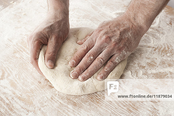 Hands working with pizza dough on a wooden floured surface
