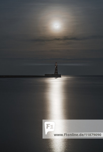 Roker Lighthouse at the end of a pier under a bright full moon reflecting on tranquil water; Sunderland  Tyne and Wear  England