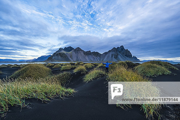 Person standing on a black sand mound looking at Vestrahorn or Stokknes on the South coast of Iceland; Hofn  Iceland