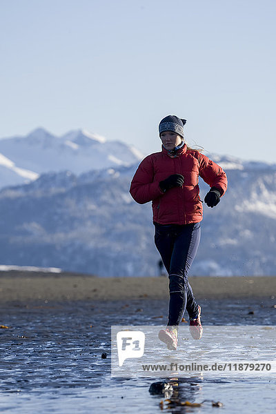 Eine junge Frau joggt im Winter am nassen Strand entlang; Homer  Alaska  Vereinigte Staaten von Amerika'.