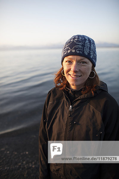 Porträt einer Frau mit roten Haaren  die eine Strickmütze trägt und am Ufer des Wassers steht; Alaska  Vereinigte Staaten von Amerika'.