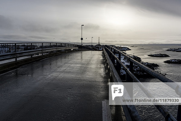 'A pier leading to the ocean with the sunlight hazy behind cloud; Lofoton Islands  Nordland  Norway'