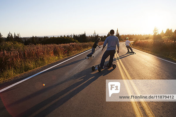 Drei junge Männer fahren bei Sonnenuntergang mit dem Skateboard eine Straße entlang; Homer  Alaska  Vereinigte Staaten von Amerika'.