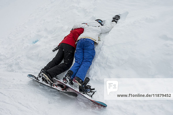 'Two young snowboarders laying together resting in the snow; Whistler British Columbia Canada'