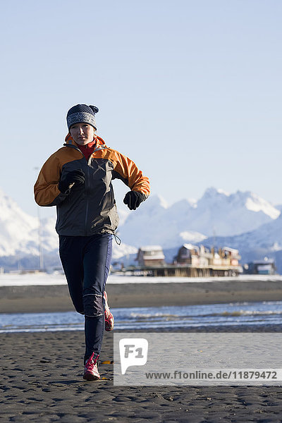 'A young woman jogs on the wet beach; Homer  Alaska  United States of America'