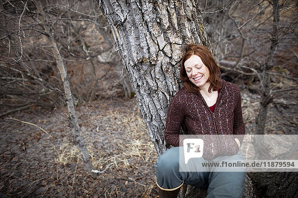Porträt einer Frau mit roten Haaren  die sich an einen Baum lehnt und mit geschlossenen Augen lächelt; Homer  Alaska  Vereinigte Staaten von Amerika'.