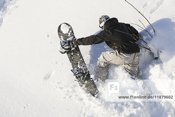 Ein Snowboarder erklimmt mit seinem Snowboard steiles Gelände im Tiefschnee; Alaska  Vereinigte Staaten von Amerika'.