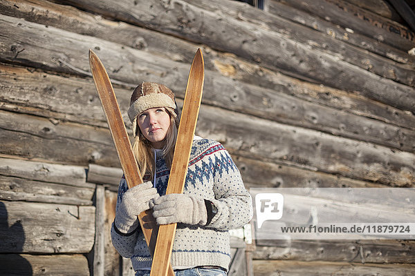 Porträt einer jungen Frau mit Holzskiern vor einer Blockhütte; Homer  Alaska  Vereinigte Staaten von Amerika'.