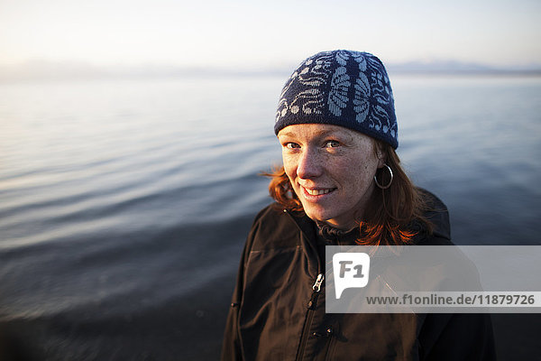 Porträt einer Frau mit roten Haaren  die eine Strickmütze trägt und mit Wasser im Hintergrund steht; Alaska  Vereinigte Staaten von Amerika