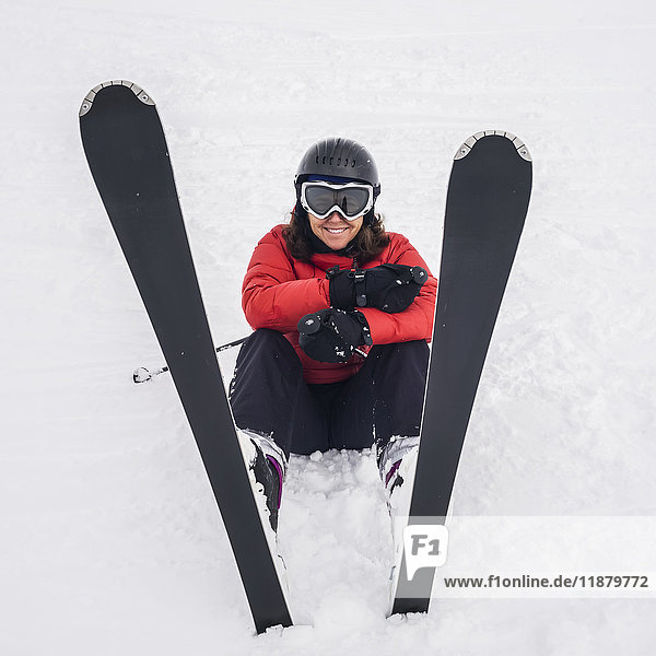 Eine Skifahrerin in einem roten Mantel sitzt mit den Skiern nach oben im Schnee; Whistler  British Columbia  Kanada'.