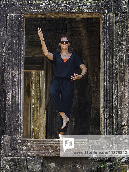 Eine Frau steht in einer Yogapose in einer Öffnung des Bayon-Tempels  Angkor Thom; Krong Siem Reap  Provinz Siem Reap  Kambodscha'.