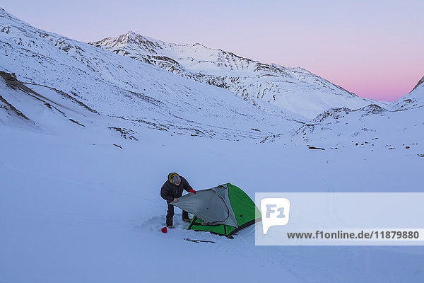 Ein Mann beim Aufbau eines Zeltes nach Sonnenuntergang während eines Wintercampingausflugs in der Alaska Range  in der Nähe des Augustana-Gletschers; Alaska  Vereinigte Staaten von Amerika'.