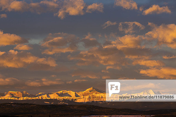 Glühend warm beleuchtete  schneebedeckte Bergkette und Vorgebirge mit leuchtenden Wolken und blauem Himmel bei Sonnenaufgang; Calgary  Alberta  Kanada
