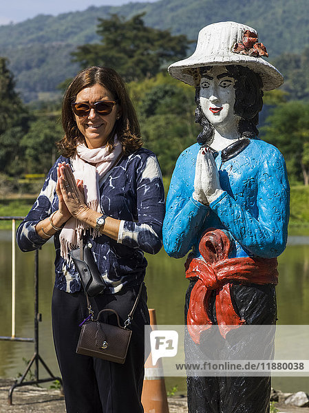 Eine Touristin posiert in einer ähnlichen Pose wie eine thailändische Statue  neben der sie steht; Tambon Pa Tueng  Chang Wat Chiang Rai  Thailand'.