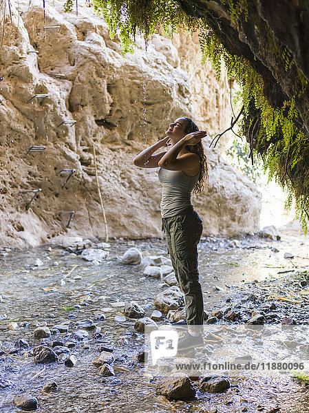 'A young woman stands on a rock and looks up along a stream at Dodim Cave  Ein Gedi Nature Reserve; South District  Israel'