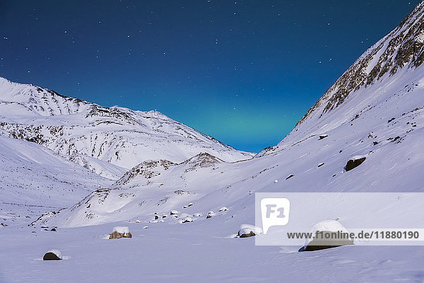 Ein sehr schwaches Band von Polarlichtern erstreckt sich zwischen den Bergen an einem abgelegenen Ort in der Alaska Range im Winter  in der Nähe des Augustana Glacier; Alaska  Vereinigte Staaten von Amerika'.