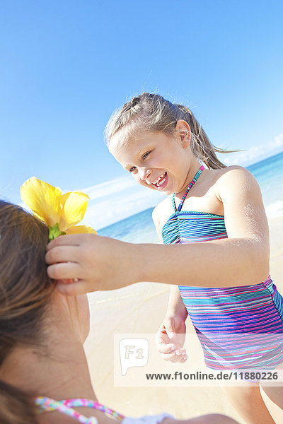 'A young girl putting a tropical flower into her mother's hair on the beach; Hawaii  United States of America'