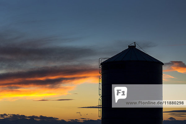 Silhouette eines großen Getreidesilos aus Metall mit bunten Wolken bei Sonnenuntergang und blauem Himmel; Alberta  Kanada'.