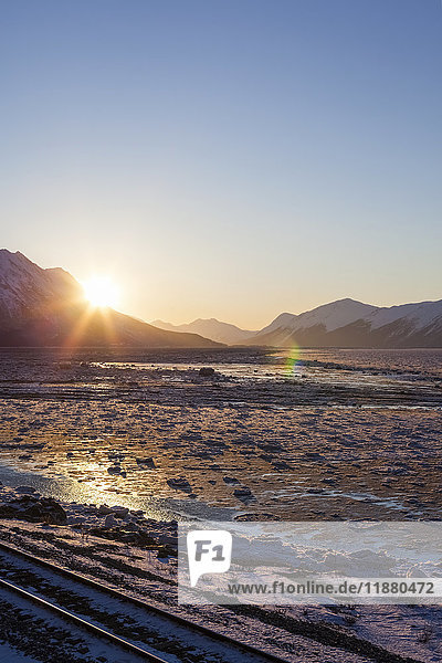Eisenbahnschienen liegen im Vordergrund  während die Sonne über den Chugach Mountains aufgeht und den eisigen Turnagain Arm beleuchtet; Alaska  Vereinigte Staaten von Amerika'.