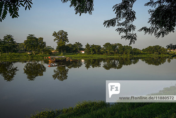 Eine ruhige Szene mit Bäumen  die sich im Flusswasser spiegeln  und einem blauen Himmel; Chiang Rai  Thailand'.