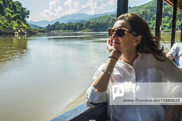 'A woman in sunglasses sits in a tour boat looking out the window while doing down the Mekong River; Luang Prabang Province  Laos'