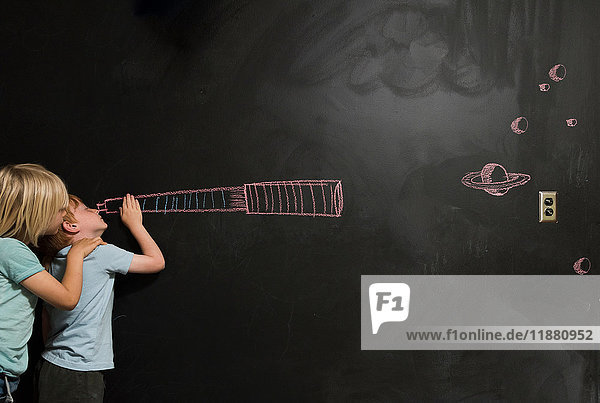 Boys looking through imaginary telescope drawn on blackboard