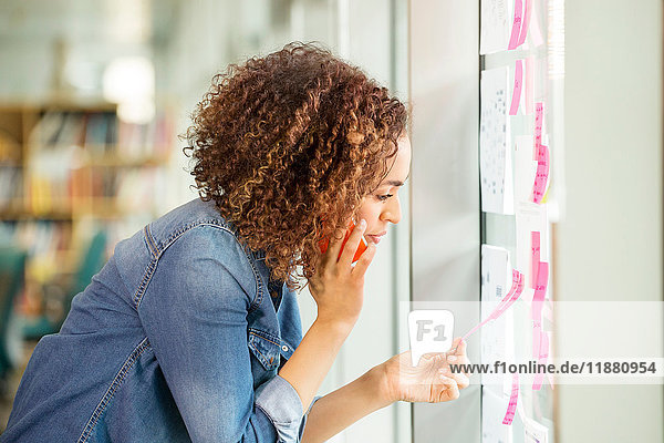 Female digital designer making phone call and looking at adhesive notes on office wall