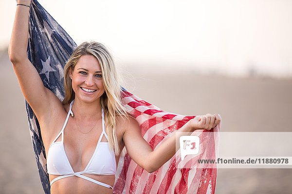 Porträt einer jungen Frau im Bikini-Oberteil  die die amerikanische Flagge hochhält  Santa Monica  Kalifornien  USA
