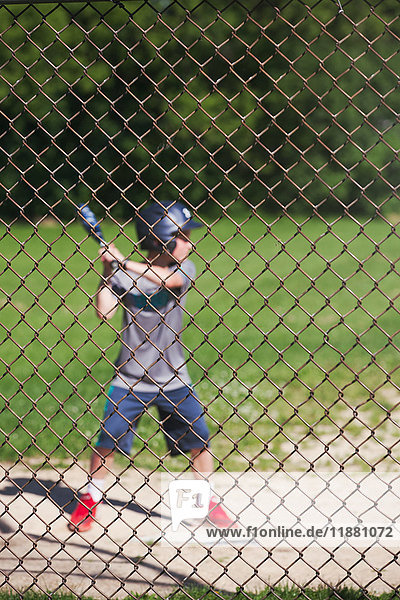 Blick durch den Maschendrahtzaun eines Baseball spielenden Jungen