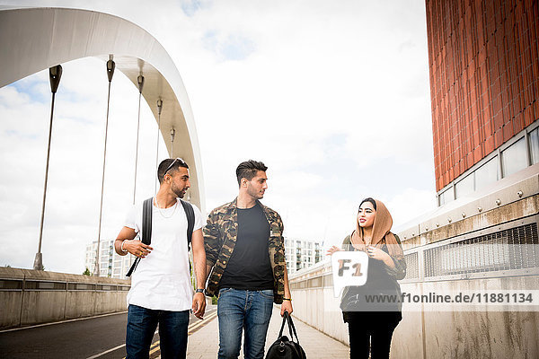 Three friends  walking across urban bridge