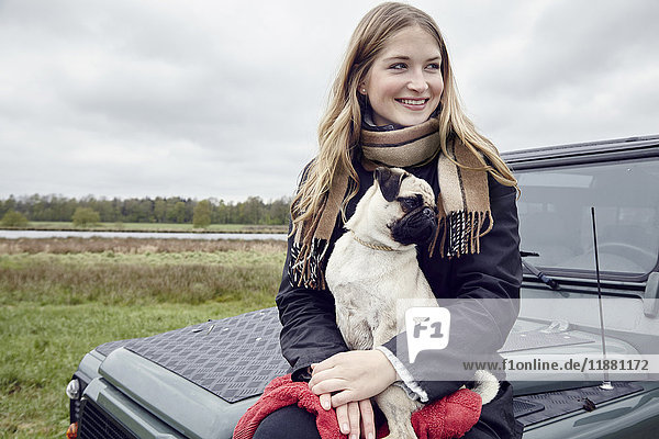 Junge Frau sitzt auf Geländewagen im Feld mit Hund auf dem Schoß